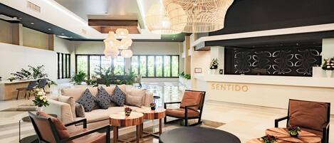 A modern lobby with a reception desk, seating area, and large windows.