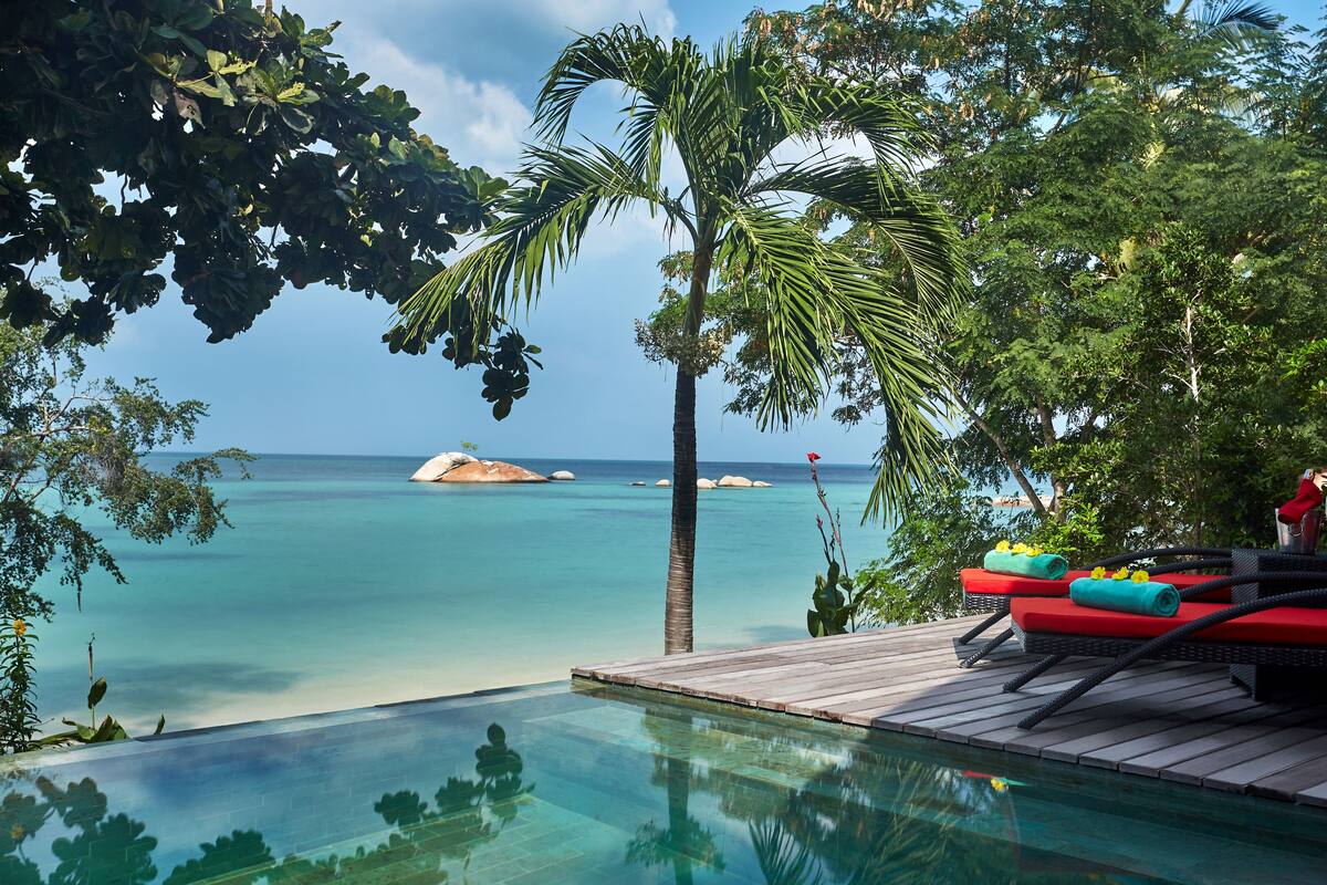 An infinity pool with a wooden deck, lounge chairs, and a view of the ocean.