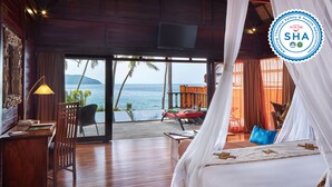 A bedroom with a bed, a desk, and a chair. There is a view of the ocean and palm trees. - Kupu Kupu Phangan Beach Villas & Spa (Ko Pha-ngan)