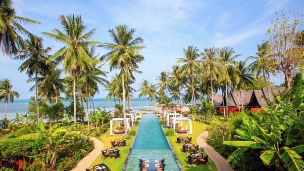 A pool with a pathway lined with tables and chairs, surrounded by palm trees and greenery, leading to a beach area. - Kupu Kupu Phangan Beach Villas & Spa (Ko Pha-ngan)