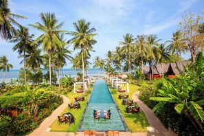 A pool with a pathway lined with tables and chairs, surrounded by palm trees and greenery, leading to a beach area. - Kupu Kupu Phangan Beach Villas & Spa (Ko Pha-ngan)