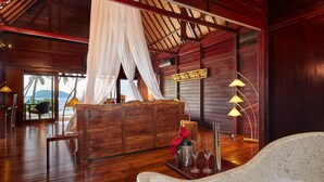 A wooden interior with a bed, a table with a bottle and glasses, and a view of the sea. - Kupu Kupu Phangan Beach Villas & Spa (Ko Pha-ngan)