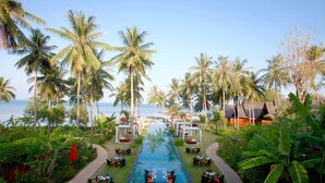A pool area with lounge chairs and tables, surrounded by palm trees and a view of the ocean. - Kupu Kupu Phangan Beach Villas & Spa (Ko Pha-ngan)