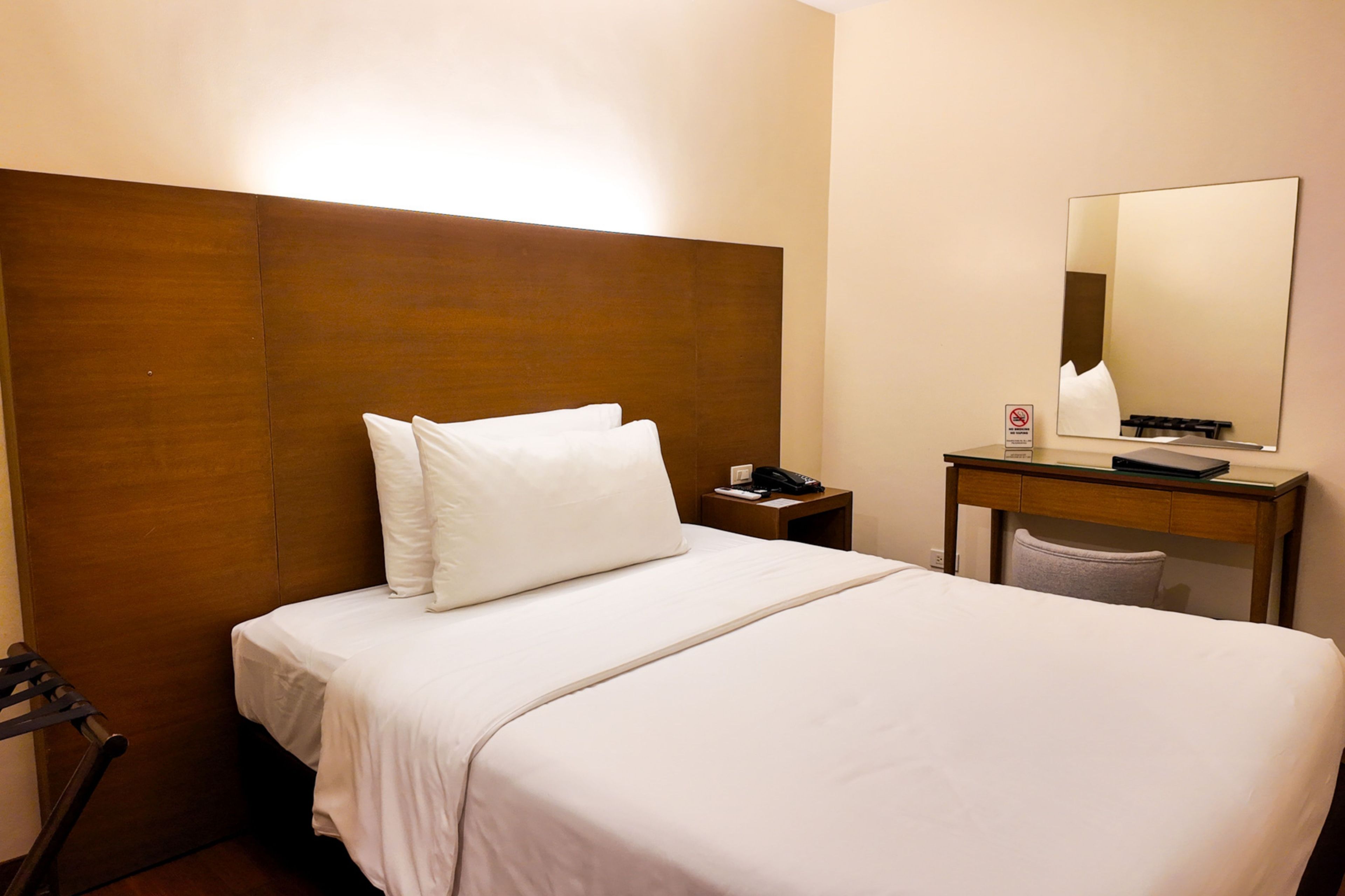 A hotel room with a bed, a nightstand, a desk, and a mirror.