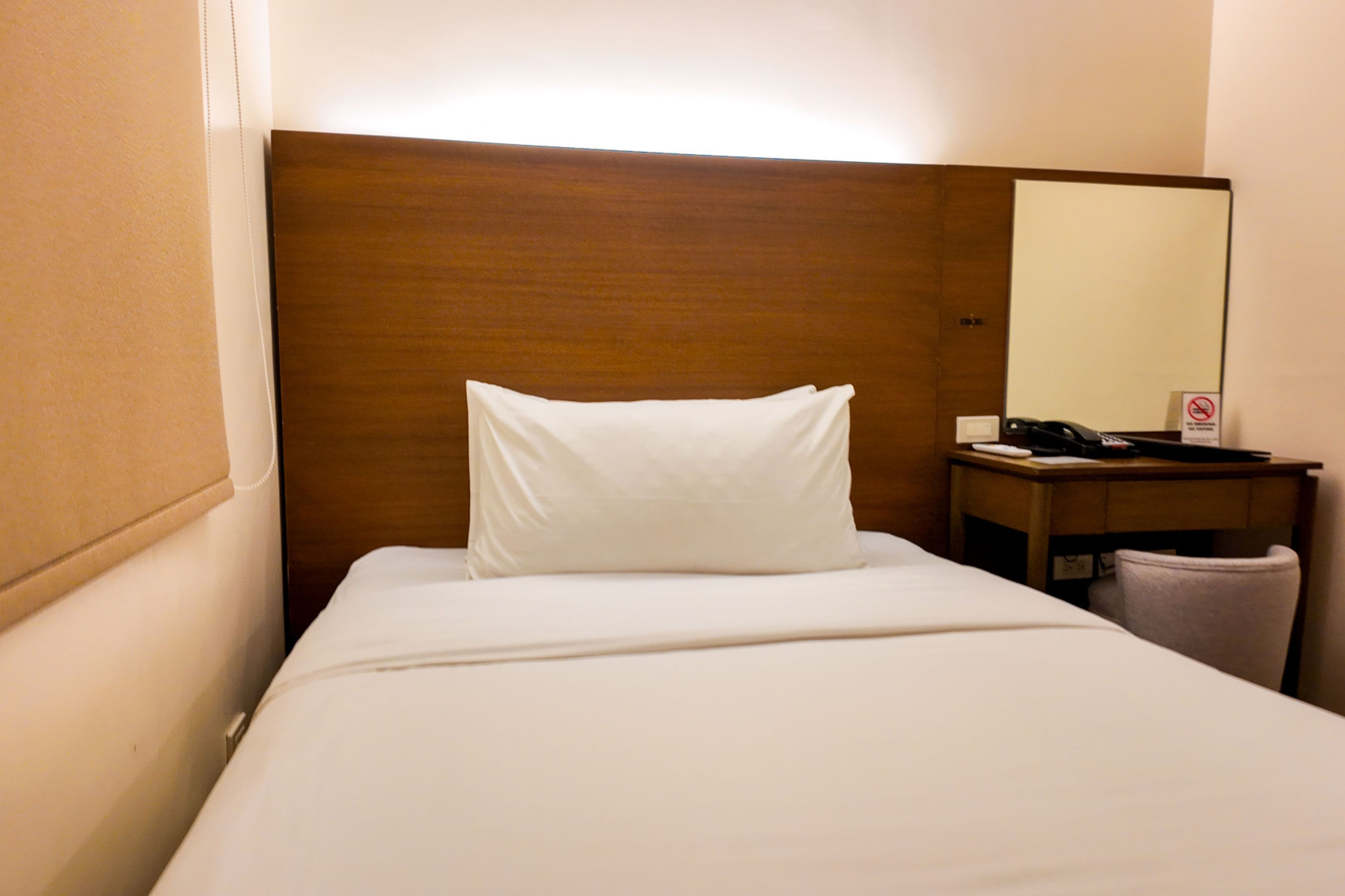 A hotel room with a neatly made bed, a wooden headboard, a bedside table with a telephone, and a mirror.