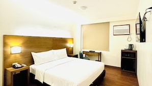 A hotel room with a wooden bed, a bedside table with a phone, a desk, and a chair. - Pearl Lane Hotel (Manila)