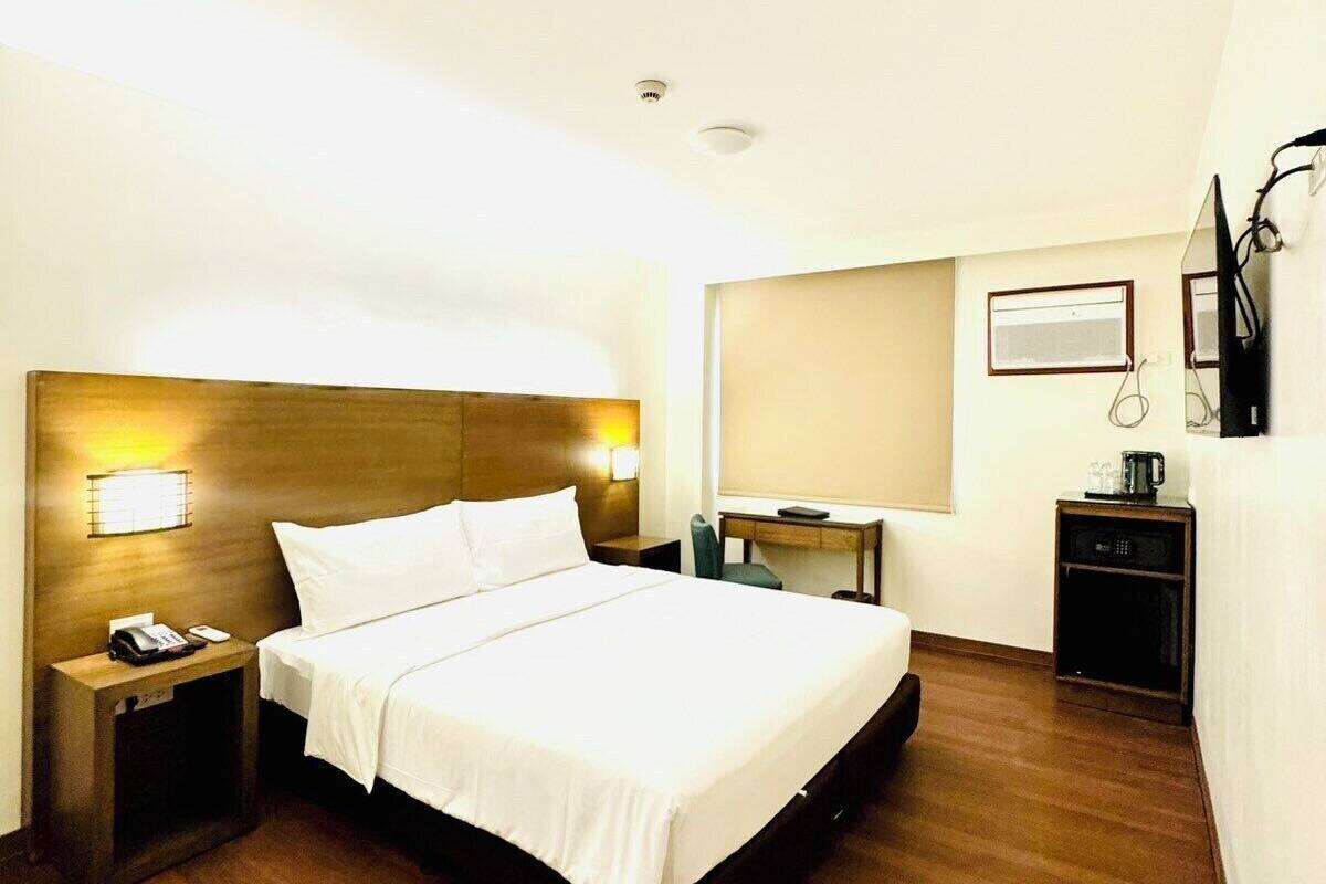 Una habitación de hotel con una cama de madera, una mesita de noche con un teléfono, un escritorio y una silla.