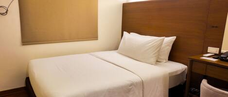 Habitación de hotel con una cama individual, cabecera de madera, mesita de noche con teléfono y una silla.