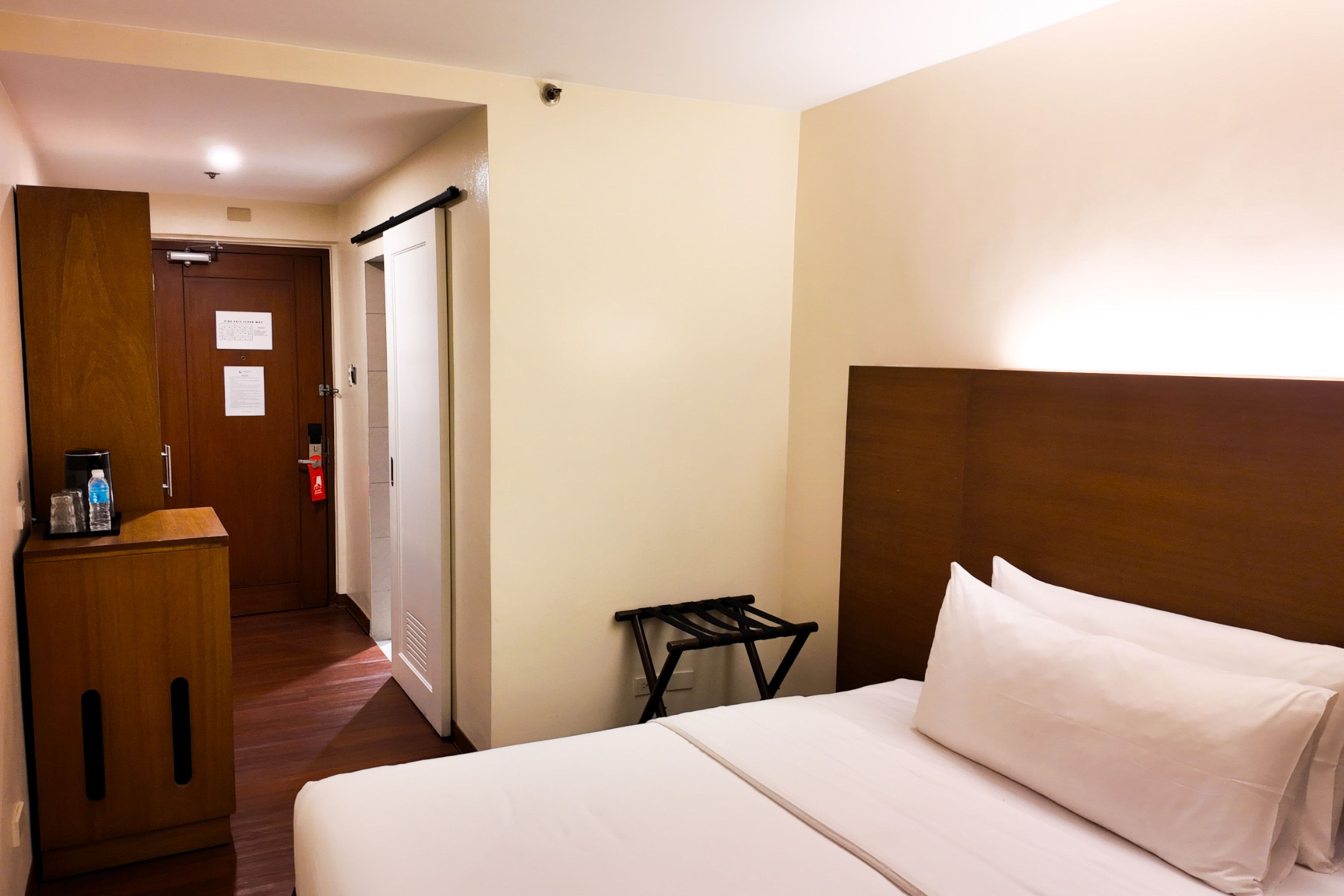 Habitación de hotel con cama, escritorio con silla, perchero y puerta que da a otra habitación.