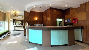 A modern reception area with a curved counter, a chandelier, and a seating area with a bench. - Pearl Lane Hotel (Manila)