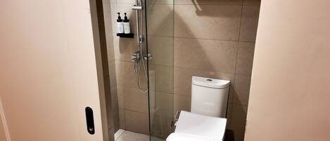 A bathroom with a glass-enclosed shower, a toilet, and a shelf with toiletries.