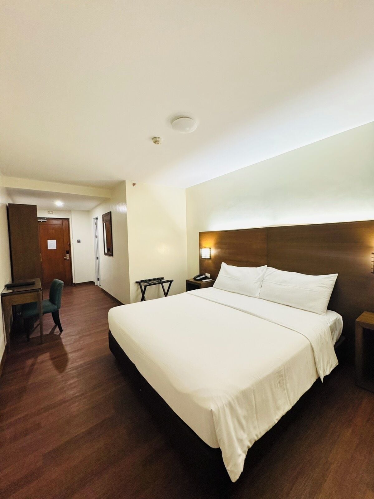 A hotel room with a large bed, a desk, a chair, and a small table.