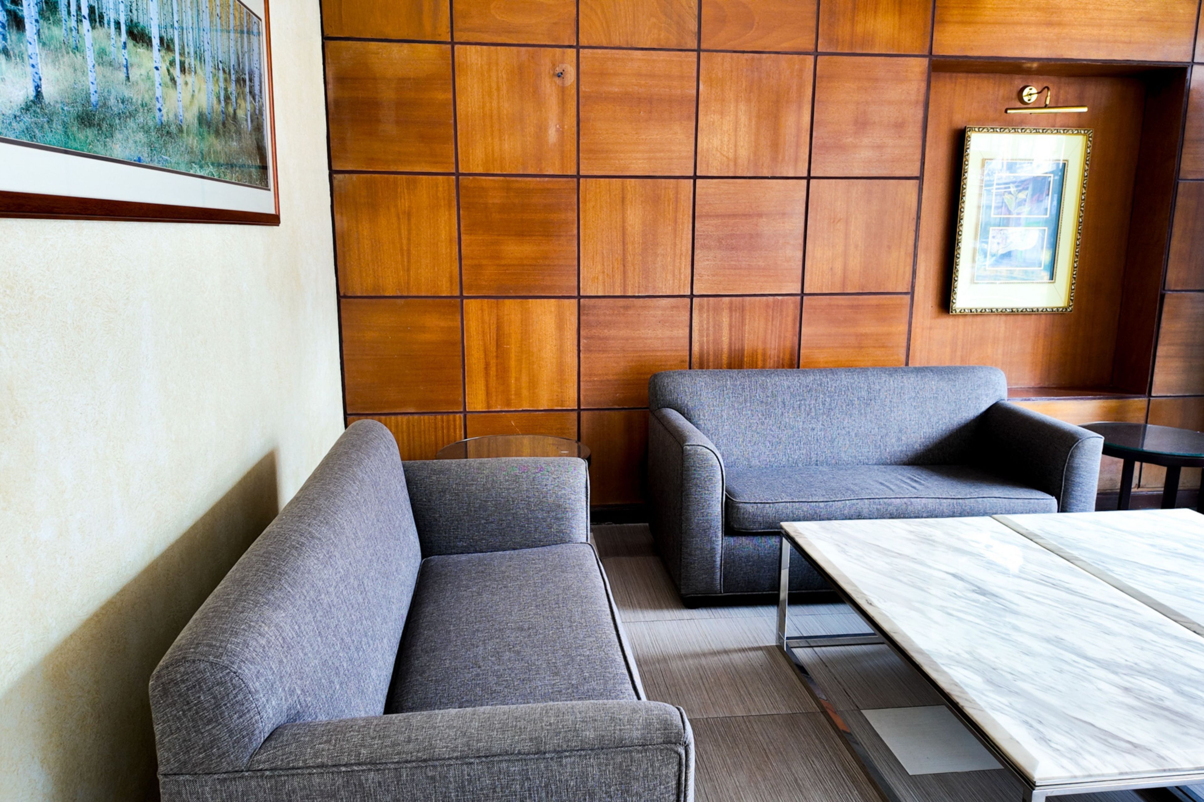 A modern interior with two grey sofas, a marble table, and wooden paneling on the walls.