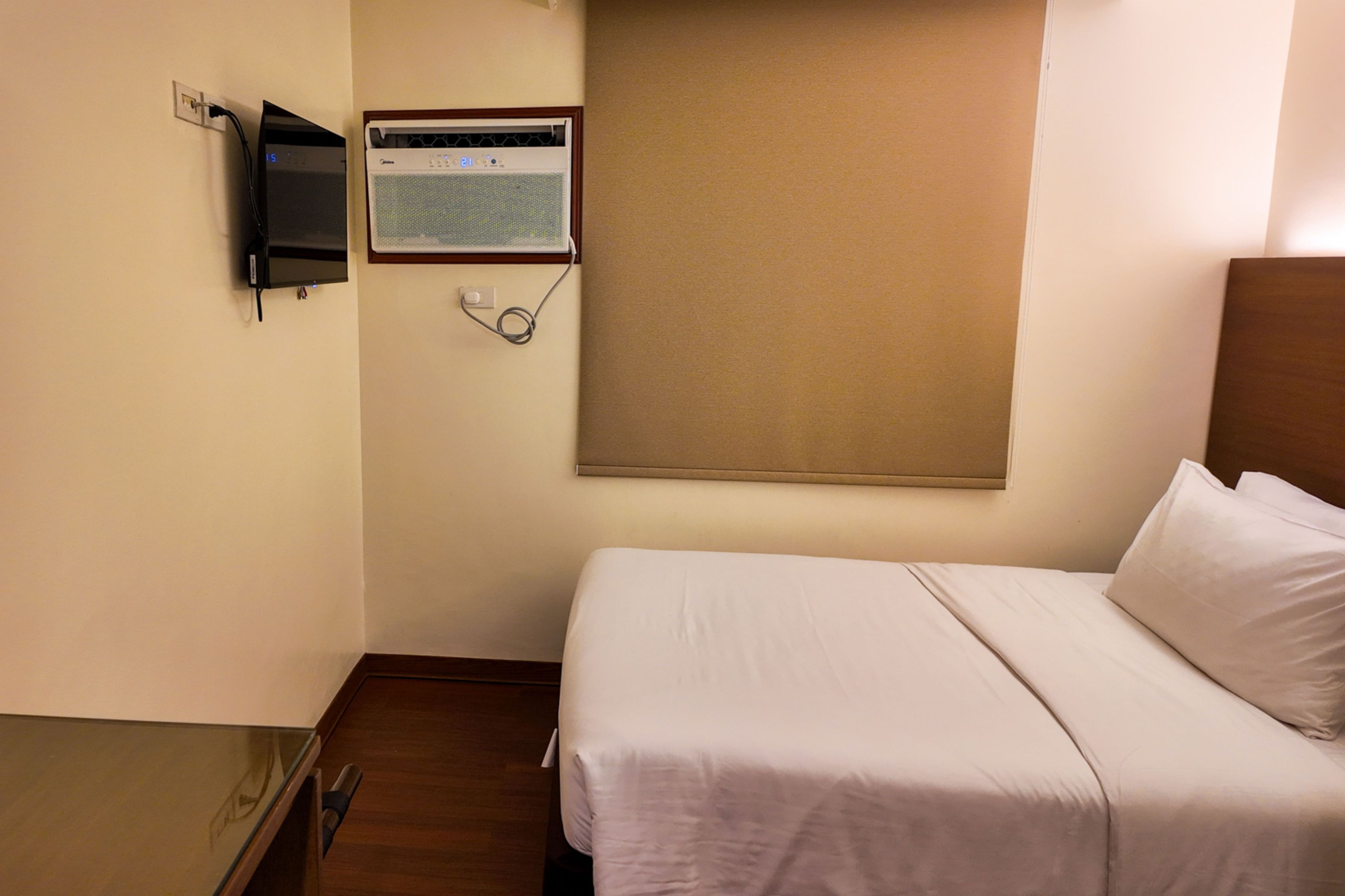 Een hotelkamer met een bed, een aan de muur bevestigde televisie en een raam met een rolgordijn.