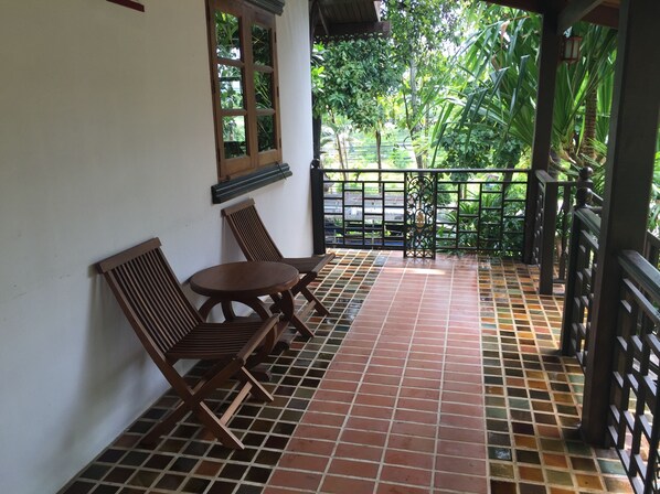 Un espacio de estar al aire libre cubierto, con suelo de baldosas, mobiliario de madera y vistas a zonas verdes.