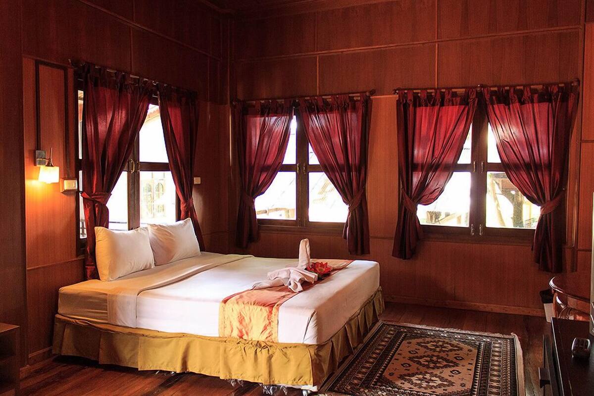 A hotel room with a large bed, wooden walls, and red curtains.