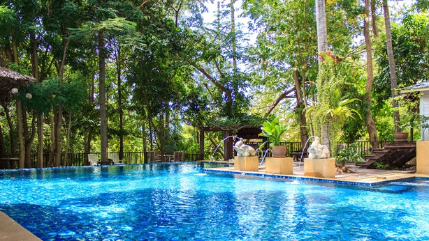 A swimming pool surrounded by lush greenery and a wooden deck with seating. - Reuan Thai Village Samui (Koh Samui)