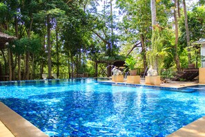 A swimming pool surrounded by lush greenery and a wooden deck with seating. - Reuan Thai Village Samui (Koh Samui)