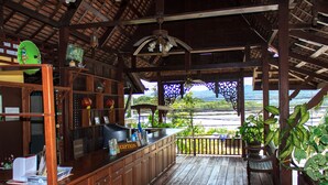 A wooden bar area with a view of the sea, a reception desk, and a ceiling fan. - Reuan Thai Village Samui (Koh Samui)