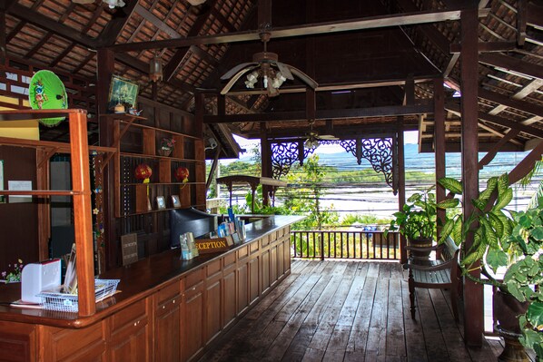 A wooden bar area with a view of the sea, a reception desk, and a ceiling fan.