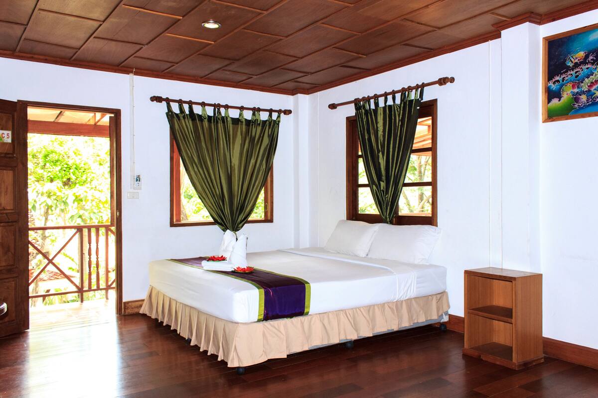 A bedroom with a bed, curtains, a nightstand, and a door leading to an outdoor area.