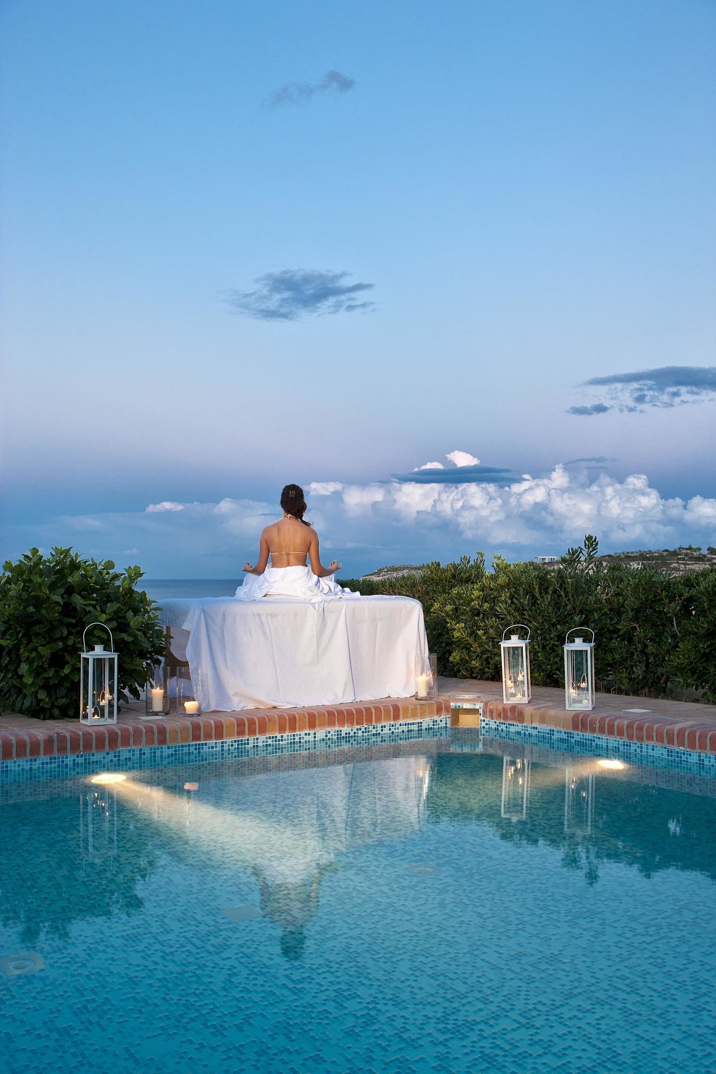 Una persona meditando junto a una piscina con vista al mar y nubes.
