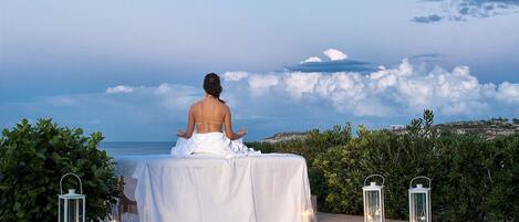 Una persona meditando junto a una piscina con vista al mar y nubes.