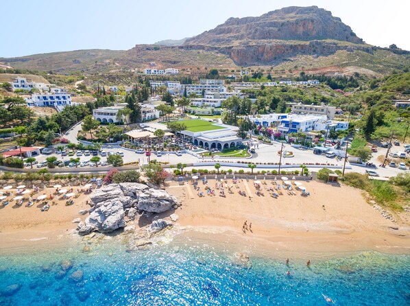 A coastal town with a beach, clear blue waters, and a mountainous backdrop. - Porto Angeli Beach Resort – All Inclusive (Rhodes)