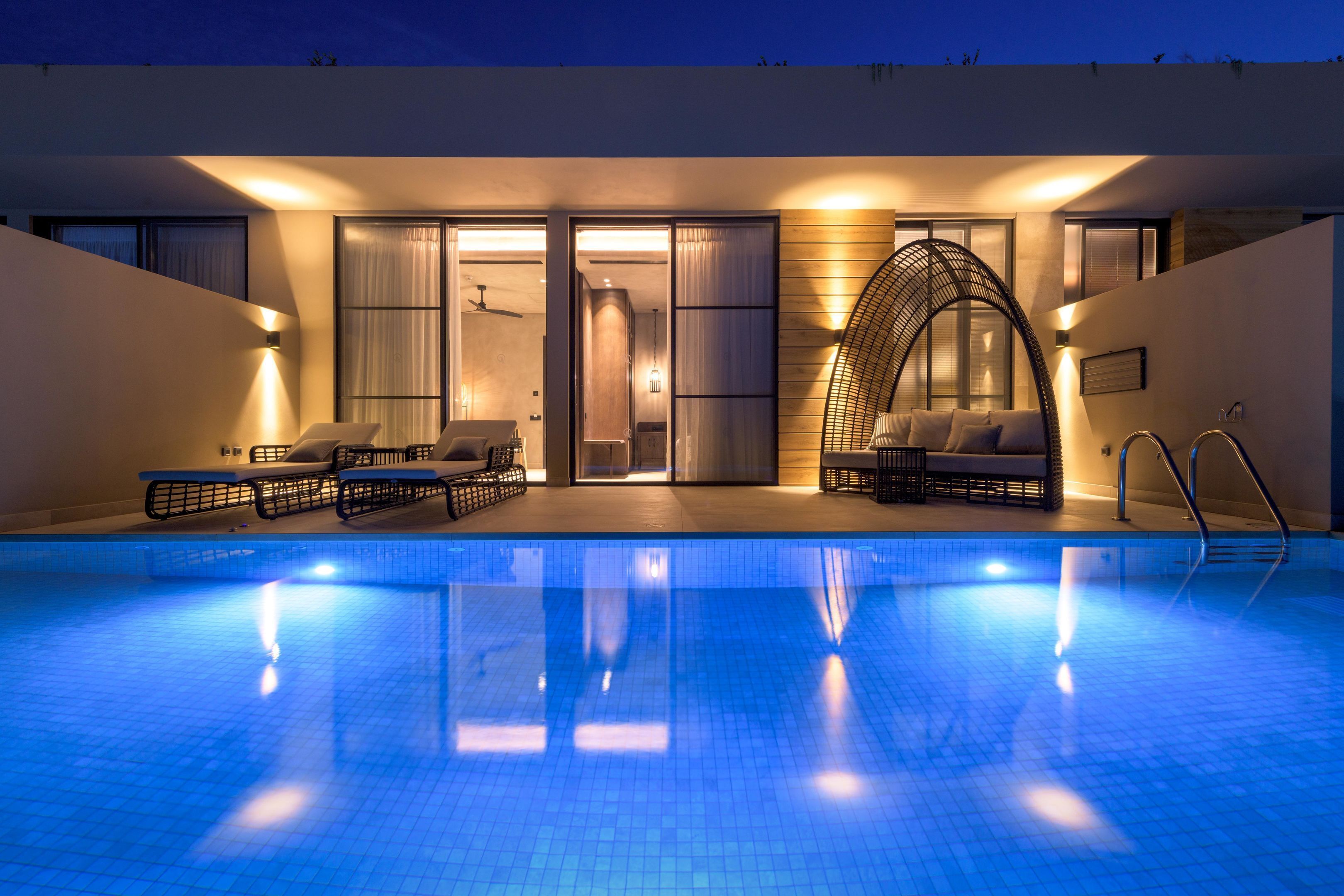 Et moderne poolområde indendørs med et klart blåt pool, liggestole og et siddeområde med et unikt, buet design.