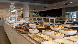 A buffet area with various food options, including cakes, pastries, and a variety of dishes in white and brown containers. - Porto Angeli Beach Resort – All Inclusive (Rhodes)