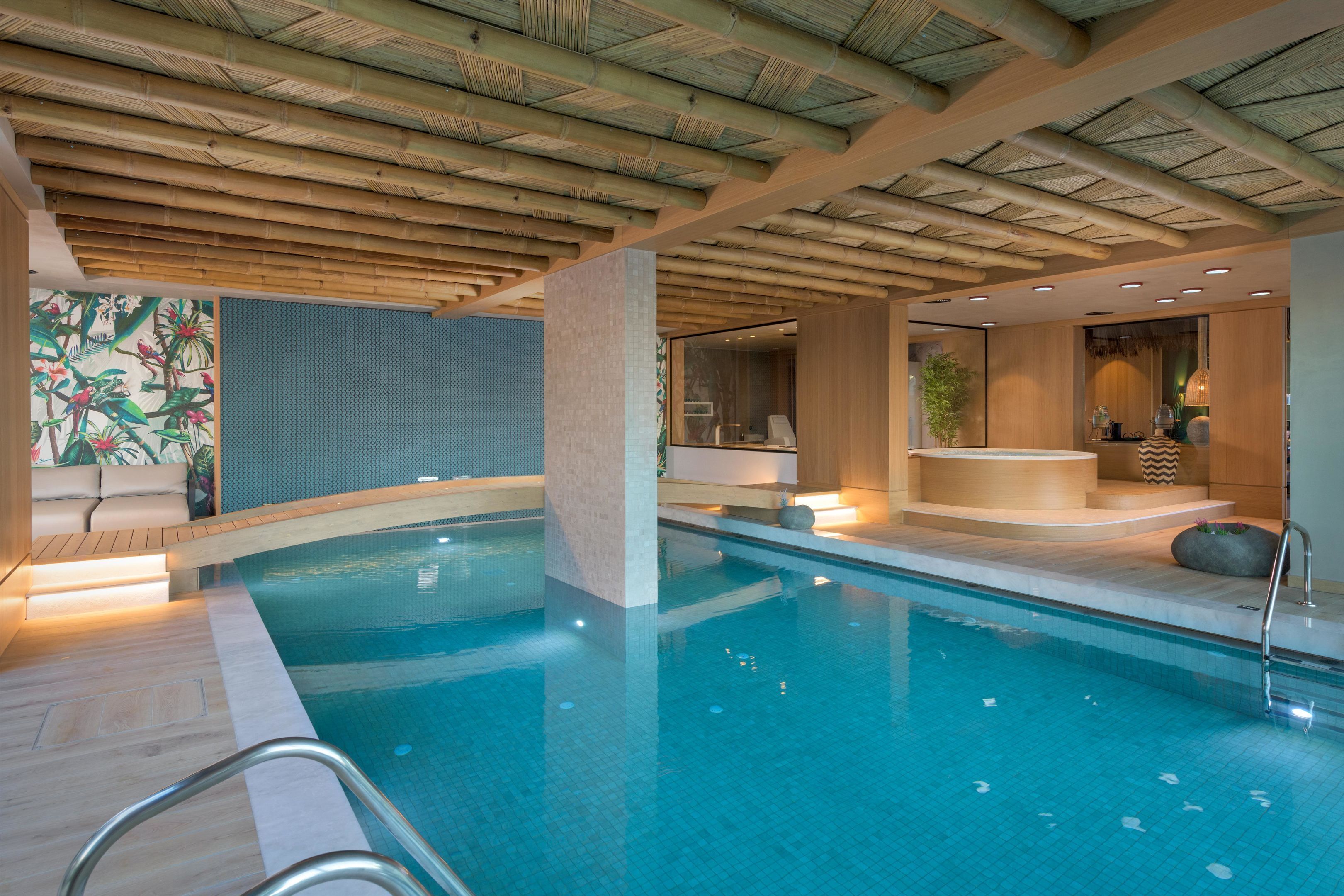 A modern indoor pool with a bamboo ceiling, a seating area with a view of the pool, and a spa-like setting with a hot tub.