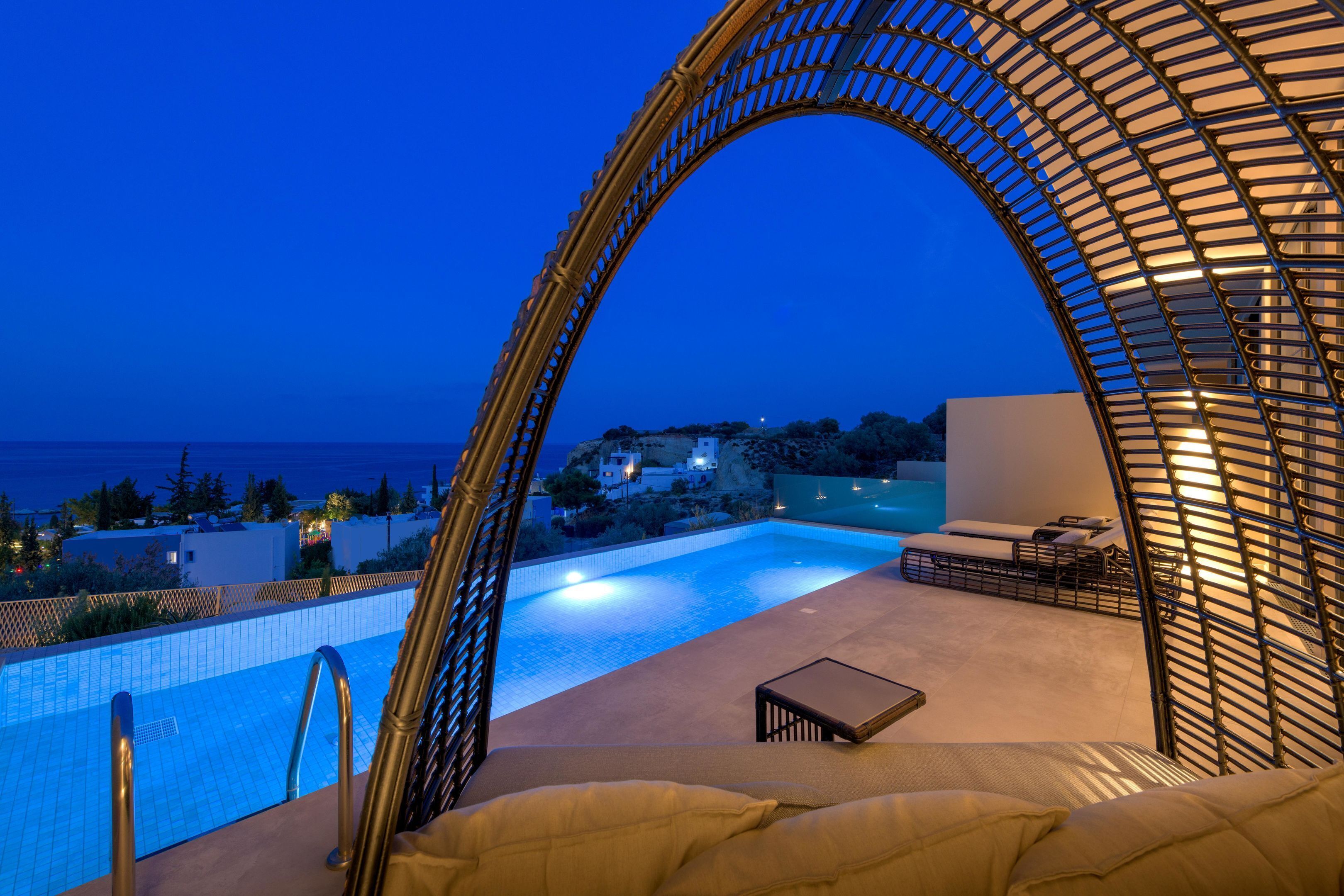 A poolside area with a view of the sea, a lounge chair, and a glass-enclosed structure.