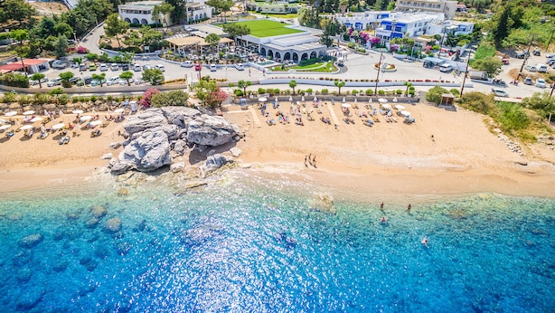 A coastal town with a beach, clear blue waters, and a mix of residential and commercial buildings. - Porto Angeli Beach Resort – All Inclusive (Rhodes)