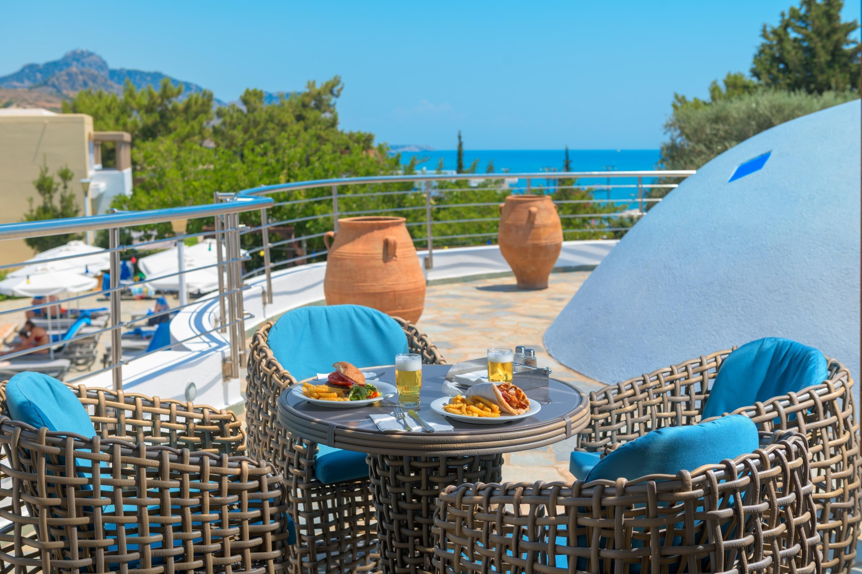 Un rincón exterior con asientos de mimbre, una mesa redonda, dos macetas de terracota y vistas al mar y a las montañas.