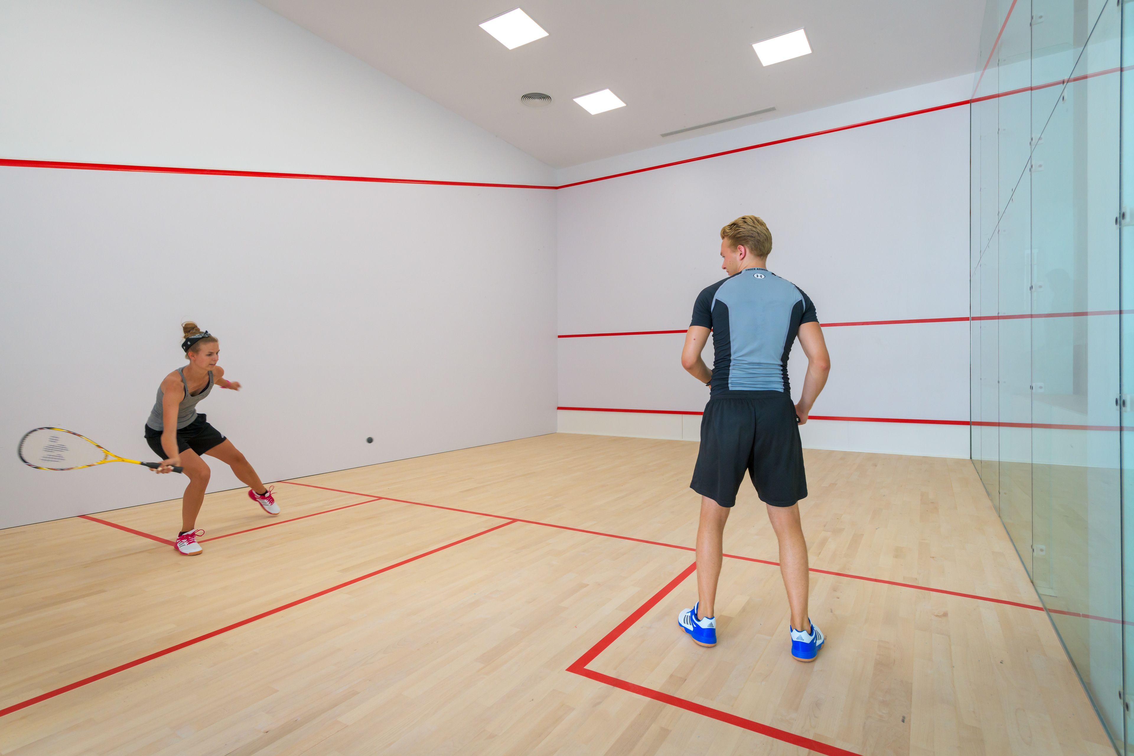 A squash court with wooden flooring and red boundary lines.