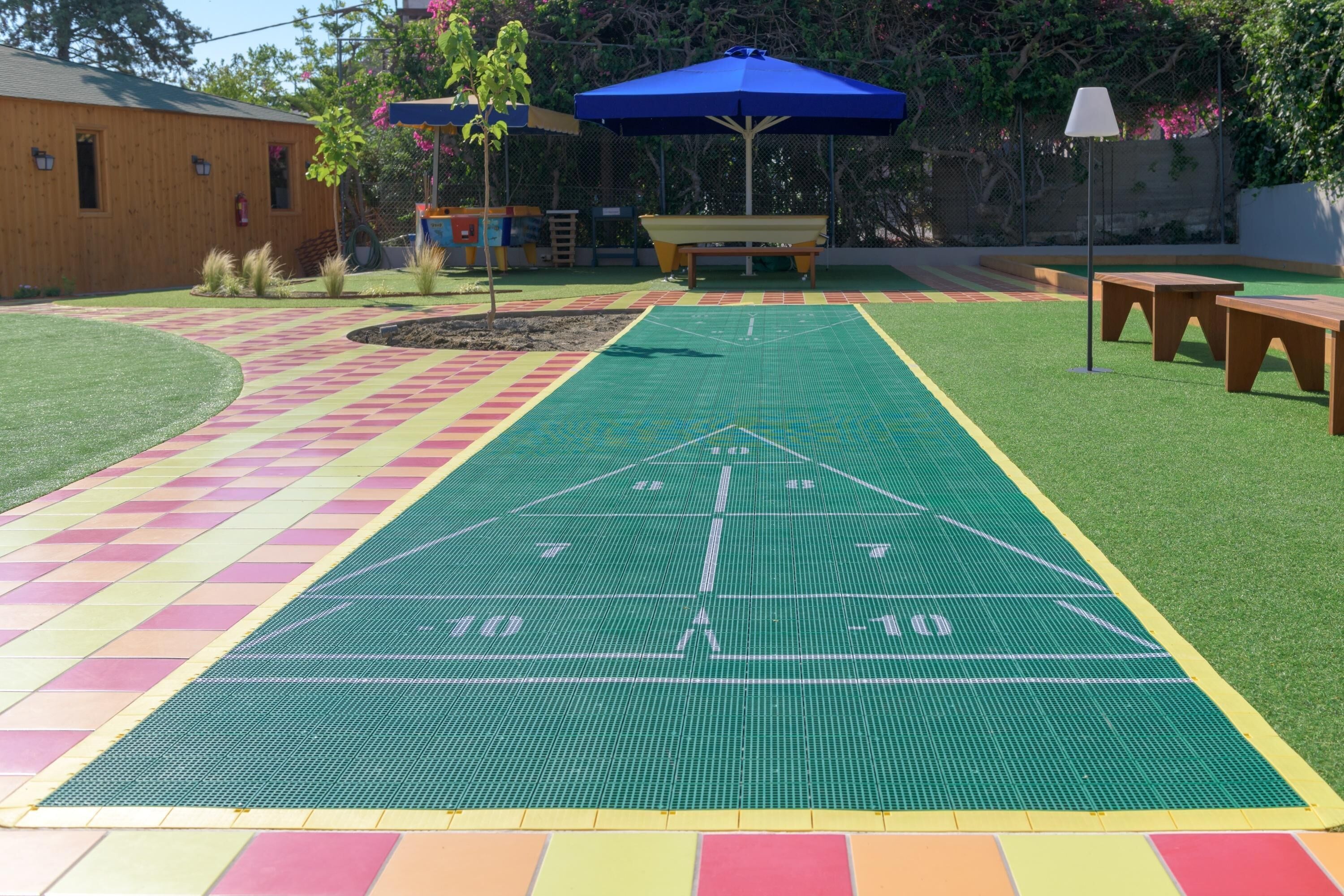 Una cancha deportiva con superficie verde, un área a cuadros amarillos y rosados, y un toldo azul.