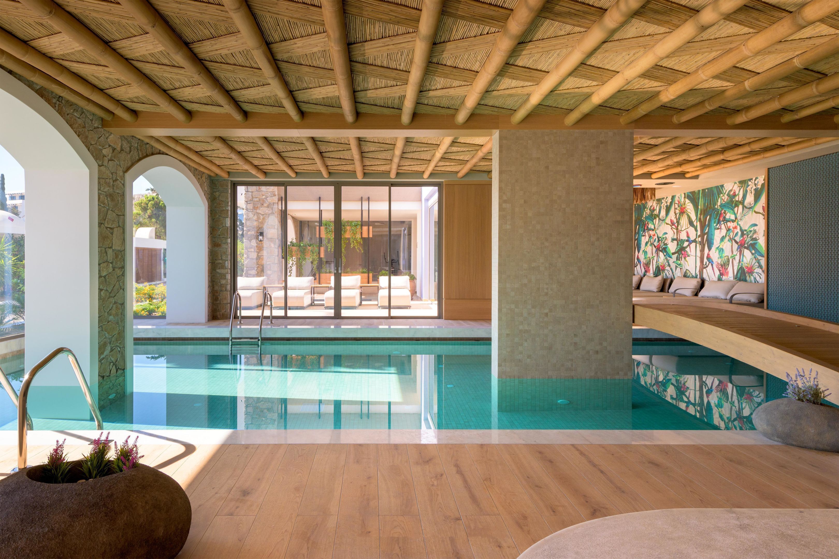 A modern indoor pool area with a bamboo ceiling, stone walls, and a view of the outdoors.