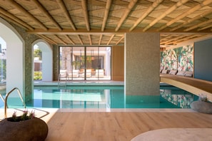 A modern indoor pool area with a bamboo ceiling, stone walls, and a view of the outdoors.