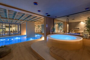 Un área interior de piscina moderna con jacuzzi, suelo de madera y paredes de vidrio.