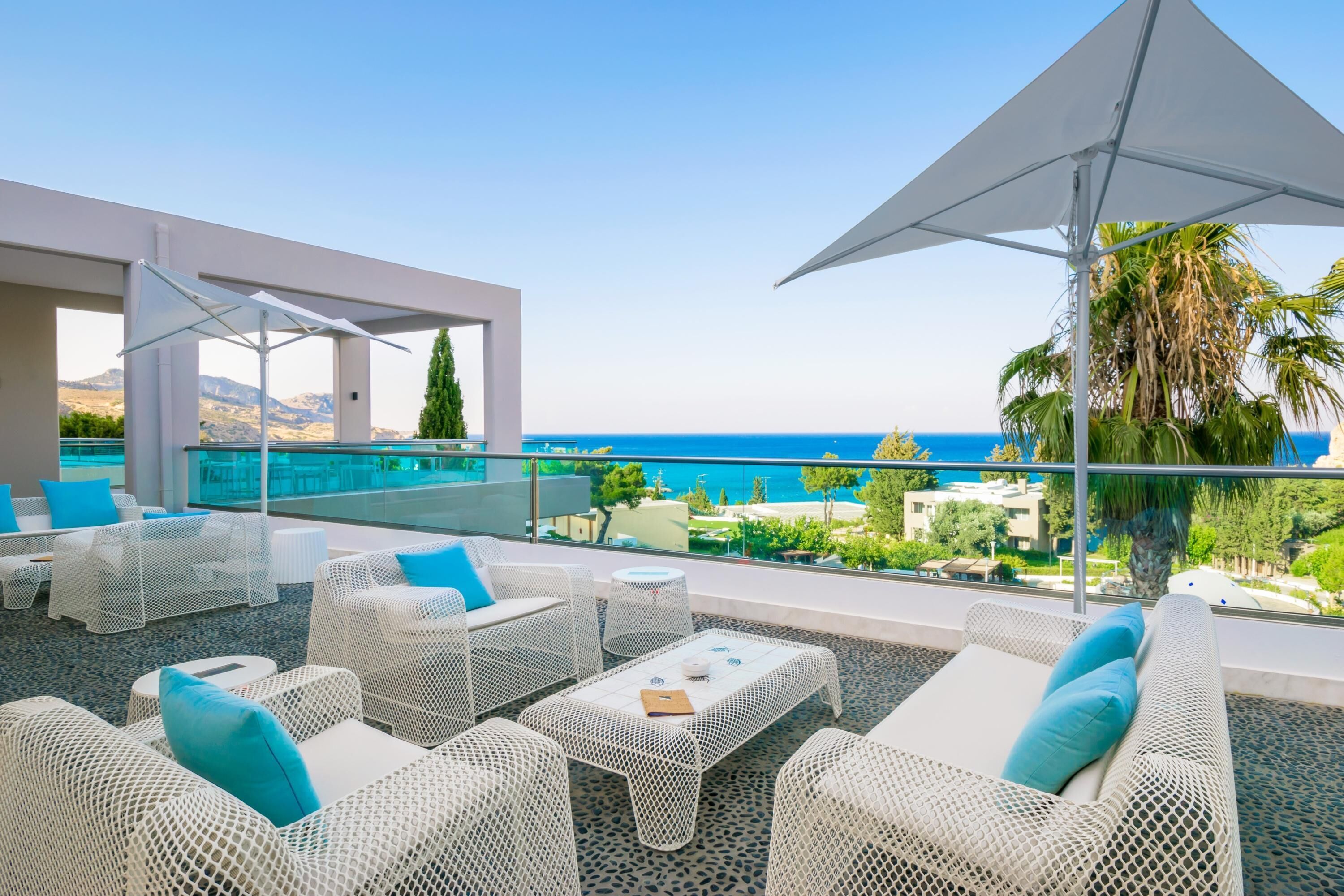 Un lounge en la azotea con mobiliario de mimbre blanco, una piscina y vistas al mar y a las montañas.
