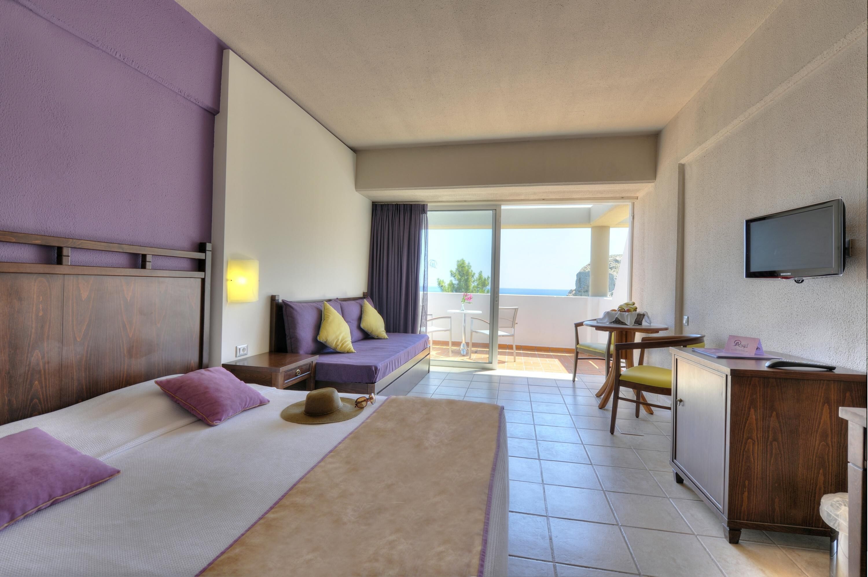 A hotel room with a bed, a desk, a TV, and a balcony with a table and chairs.