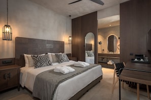 A modern hotel room with a large bed, bedside tables, a dining area, and a bathroom with a mirror and shower.