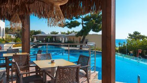 A poolside area with wicker furniture and a view of the pool. - Porto Angeli Beach Resort – All Inclusive (Rhodes)