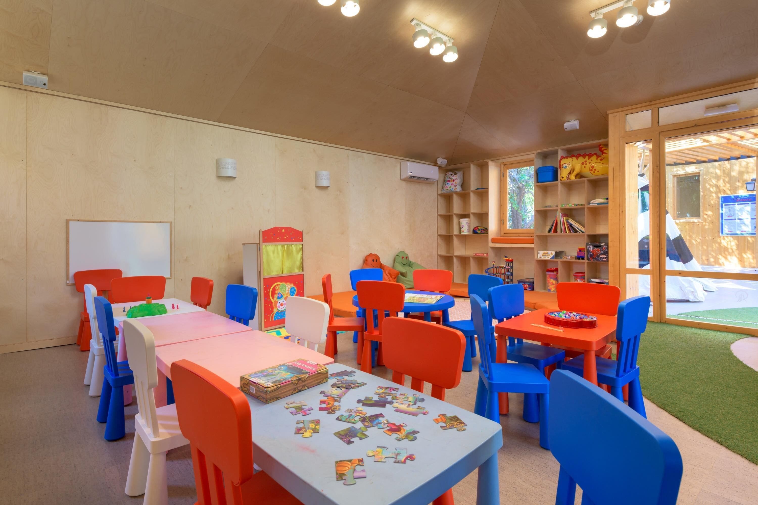 Una sala de juegos infantiles con mesas, sillas, rompecabezas y juguetes.