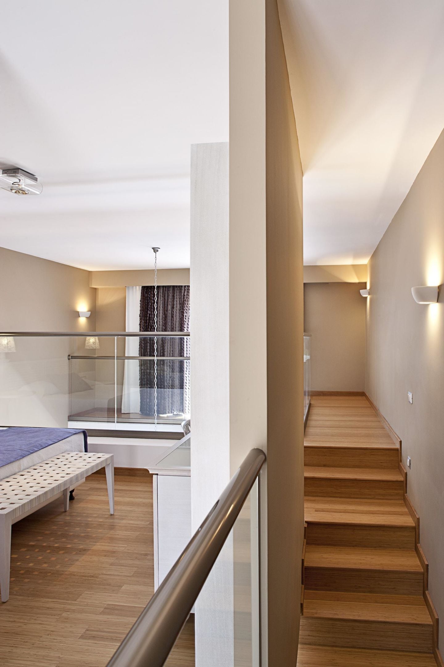 Un interior moderno con una escalera, una cama y un ventanal con cortinas.