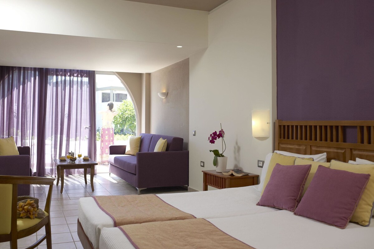A hotel room with a bed, two bedside tables, a sofa, a chair, and a dining table.