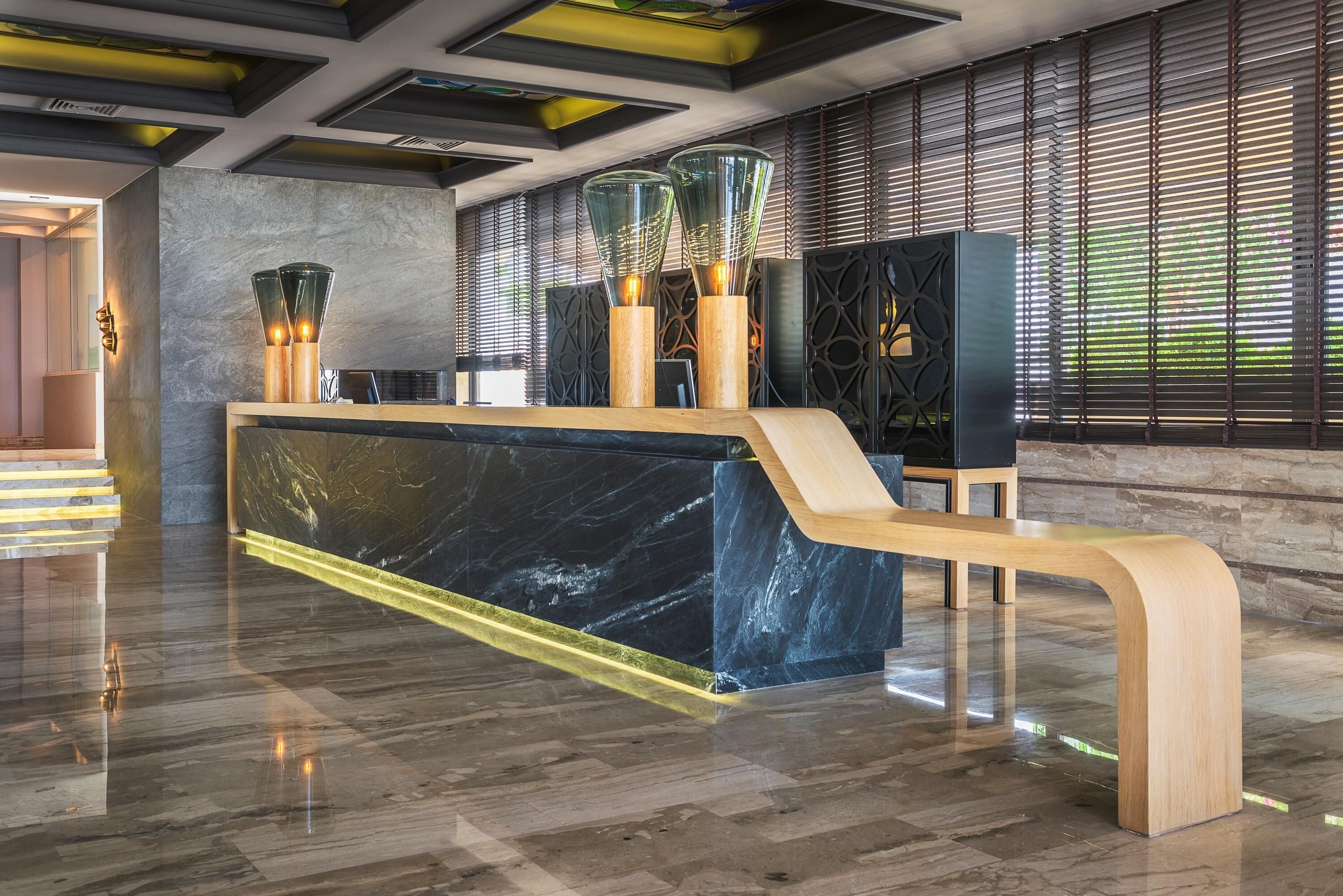 Una moderna recepción con encimera de mármol, banco de madera y lámparas de vidrio decorativas.
