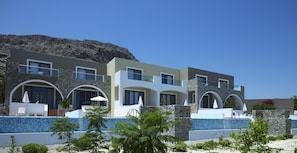 A modern multi-story hotel with stone facades, balconies, and a pool area. - Porto Angeli Beach Resort – All Inclusive (Rhodes)