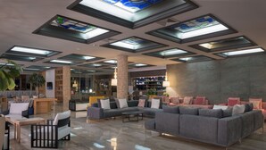 A spacious lobby with a large grey sectional sofa, a wooden coffee table, and a brick pillar. - Porto Angeli Beach Resort – All Inclusive (Rhodes)