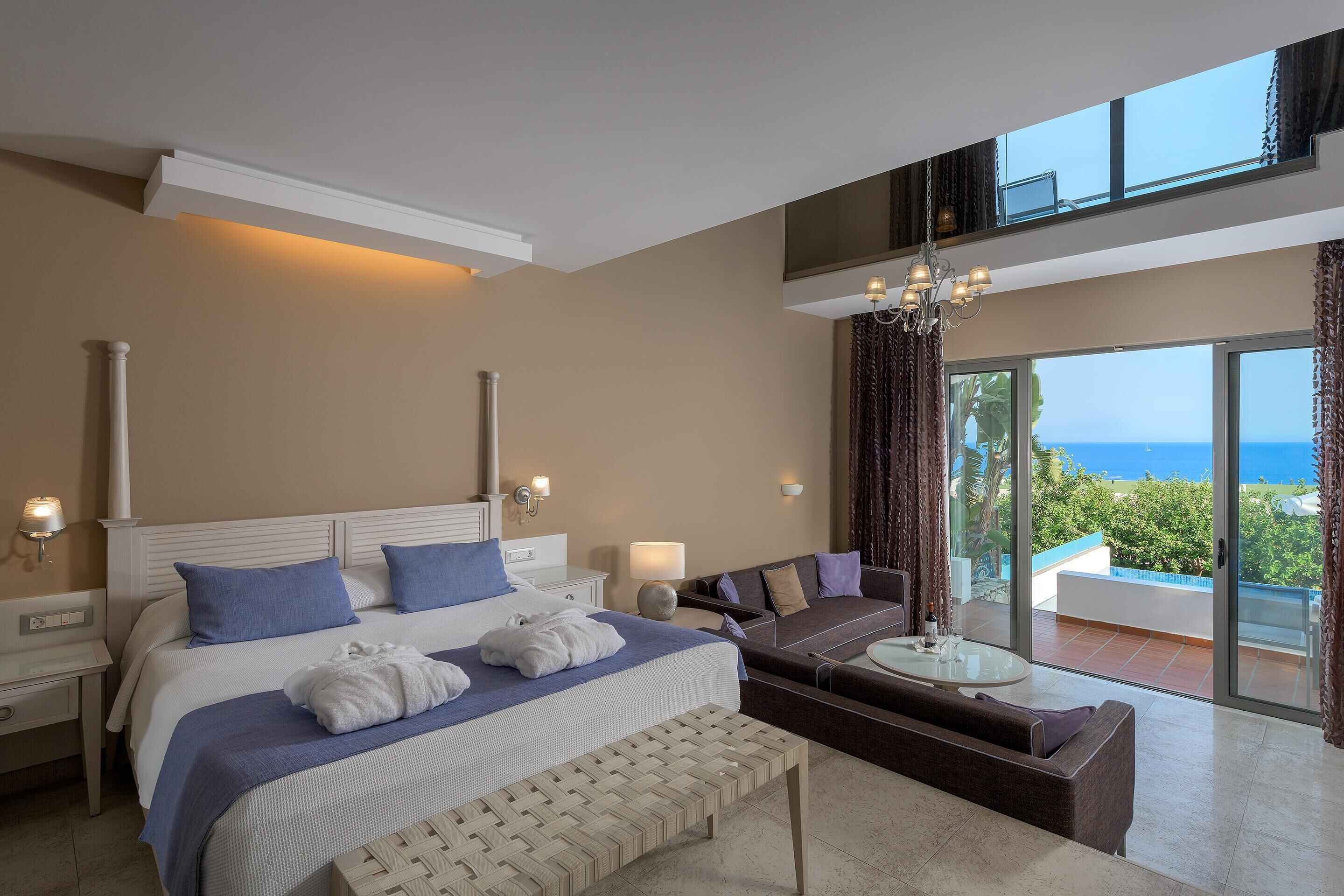 A spacious bedroom with a large bed, a sofa, and a balcony with a view of the sea.